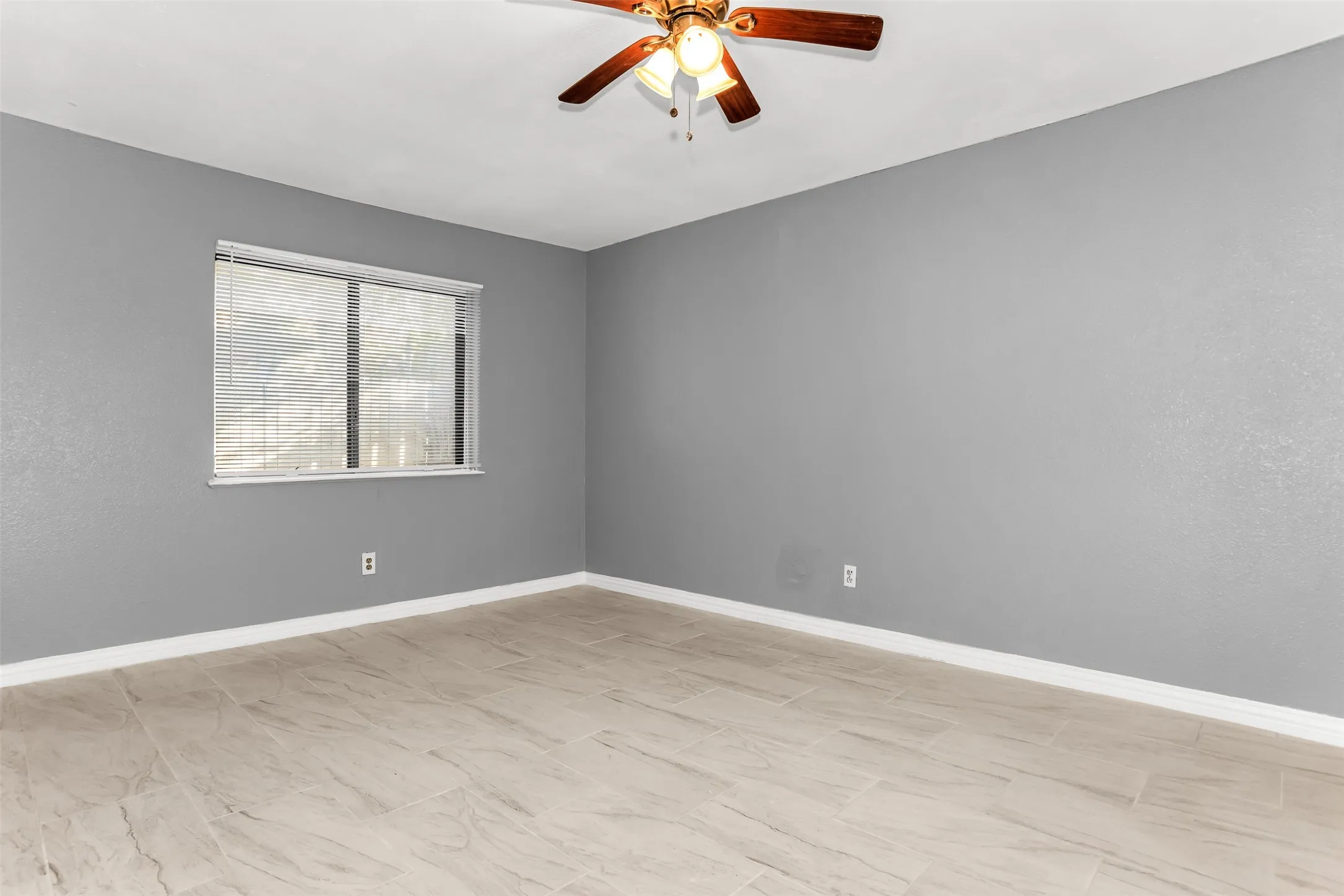Recessed window with horizontal blinds, wood-finish ceiling fan, and light-toned tile flooring