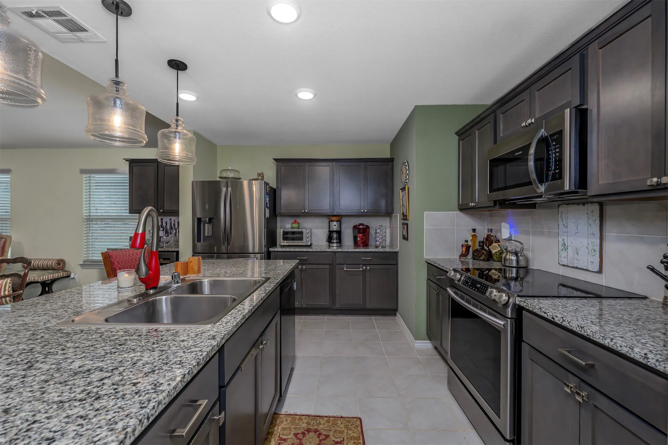 Kitchen featuring granite countertops, stainless steel appliances, dark wood-finish cabinetry, a double basin sink, and recessed lighting