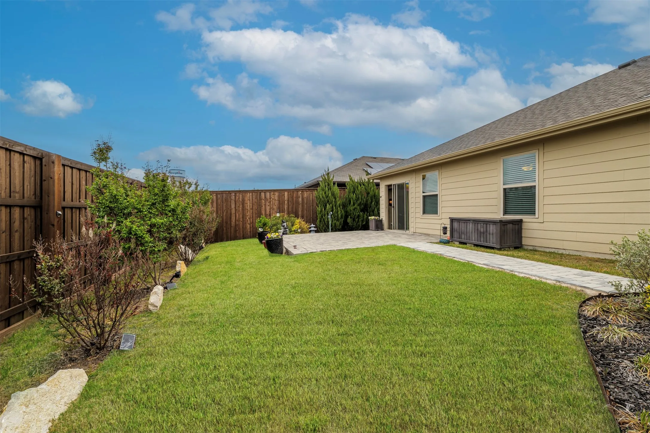 Expansive backyard featuring a manicured lawn, full privacy fencing, and a paver patio