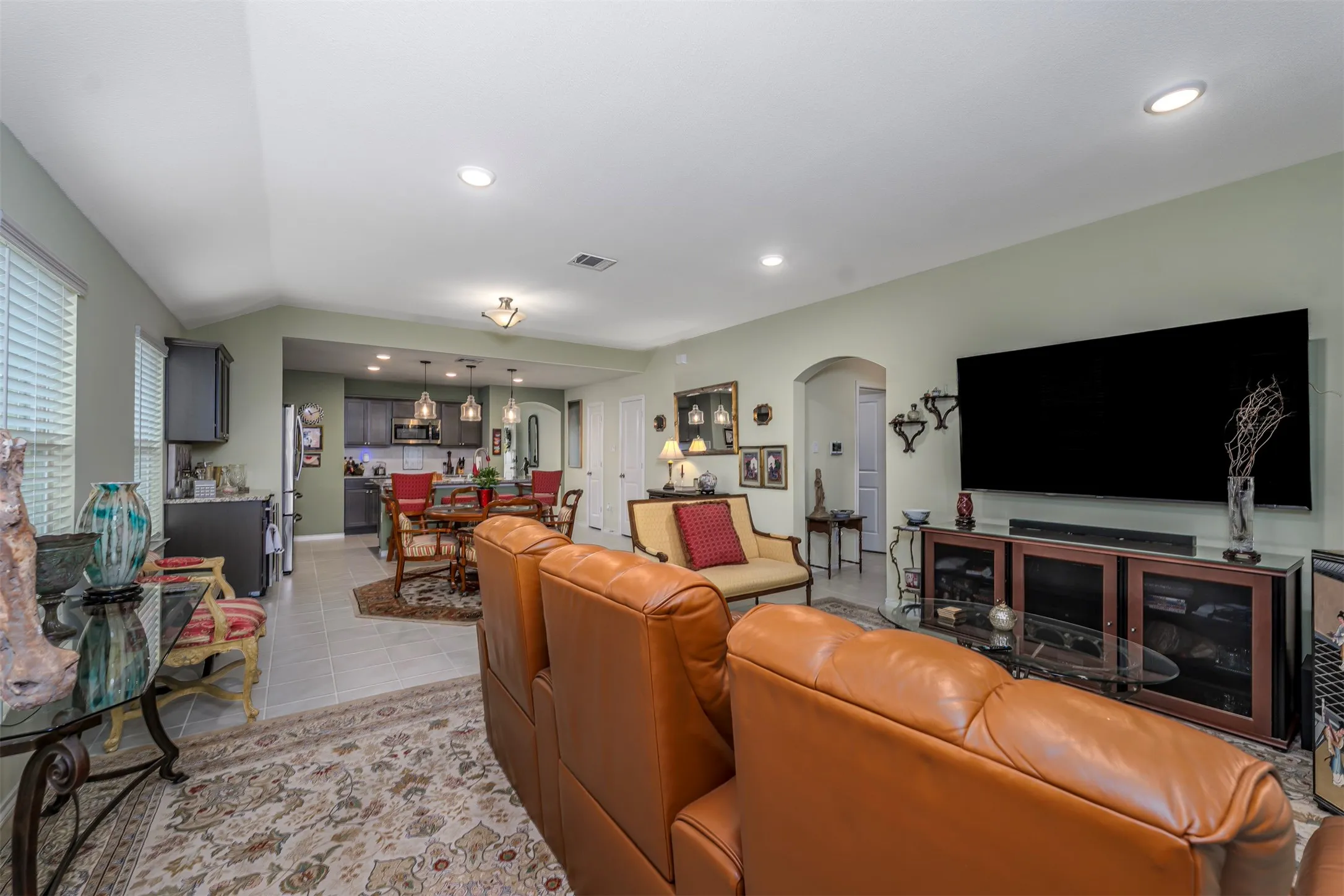 Open-concept living space featuring recessed lighting, light-toned tile flooring, and a kitchen with dark cabinetry and pendant lighting