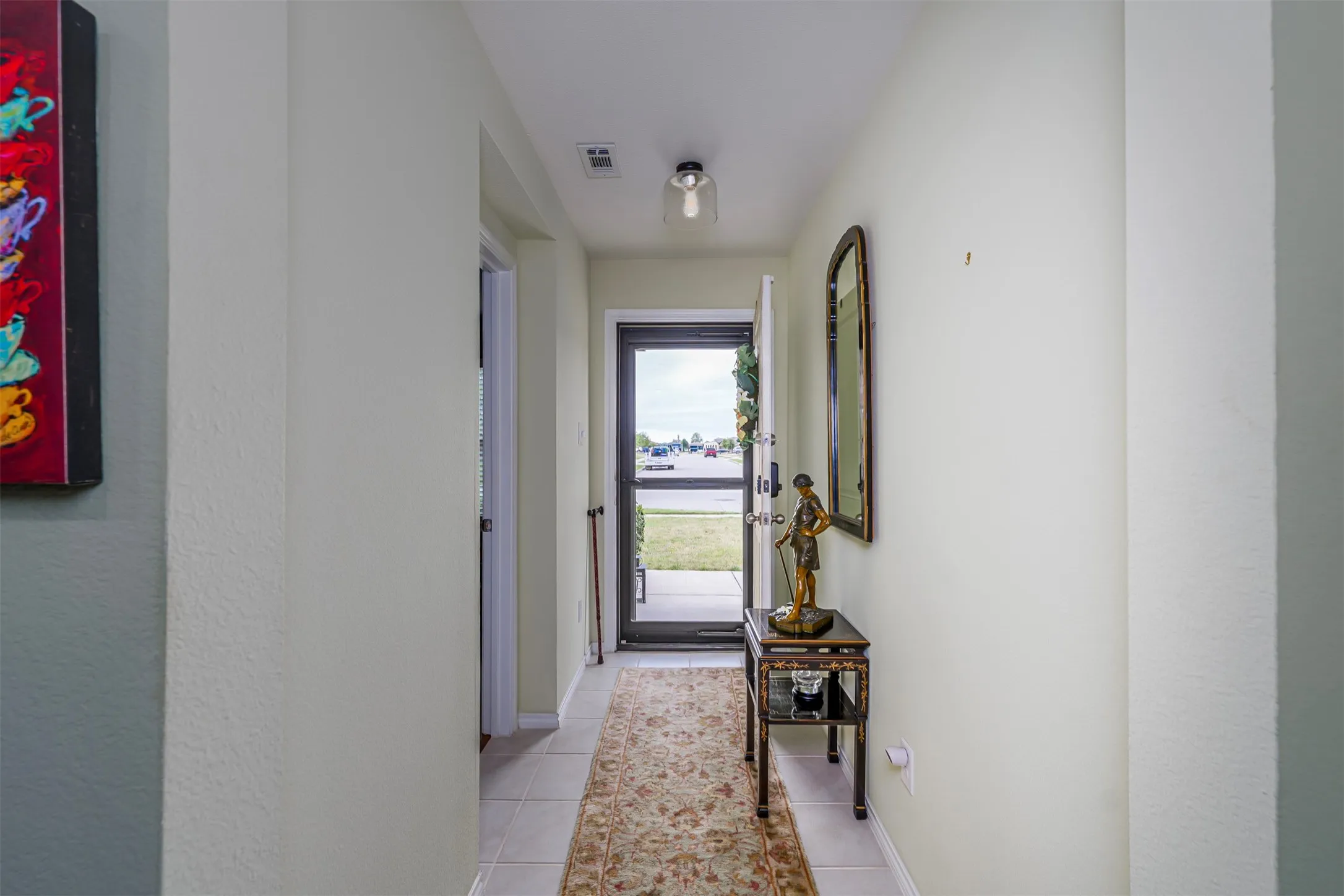 Tiled entry hallway featuring a glass-paneled front door, overhead lighting, and an additional interior doorway