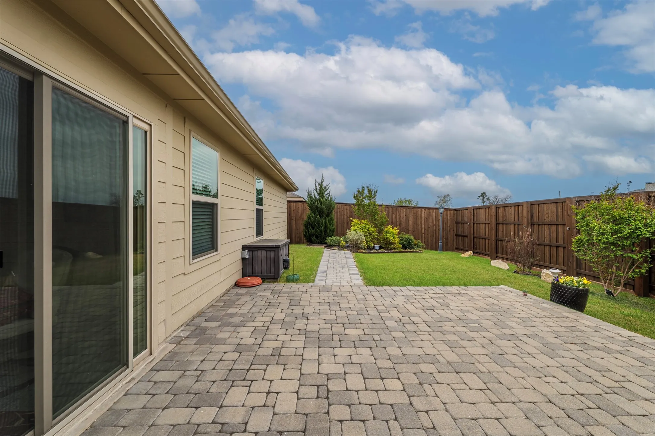 Expansive paver patio extending from the home's sliding glass doors, featuring a geometric stone pattern and seamless integration with the manicured lawn