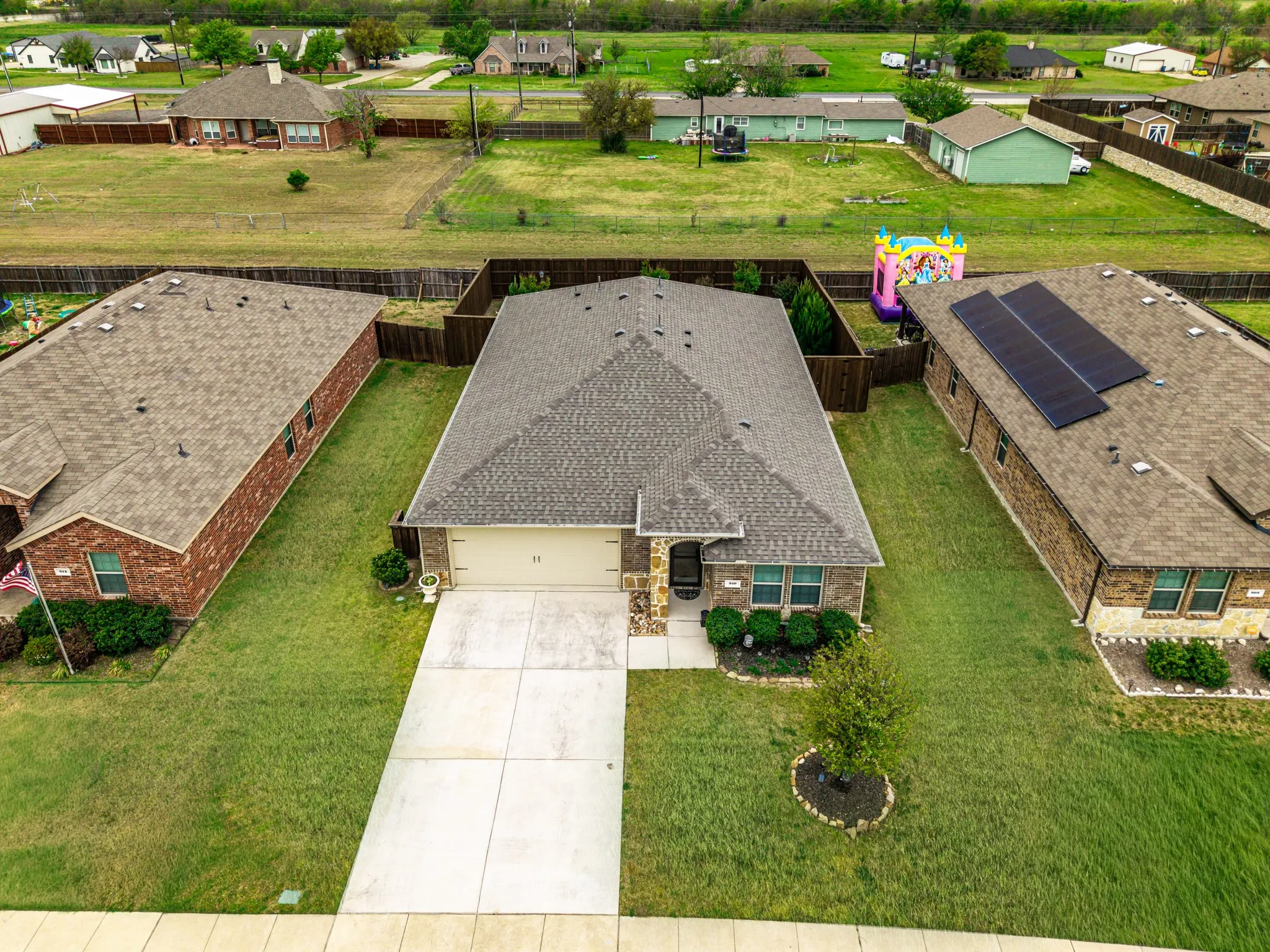 Brick and stone facade, attached two-car garage, concrete driveway, front yard landscaping, and a fenced backyard