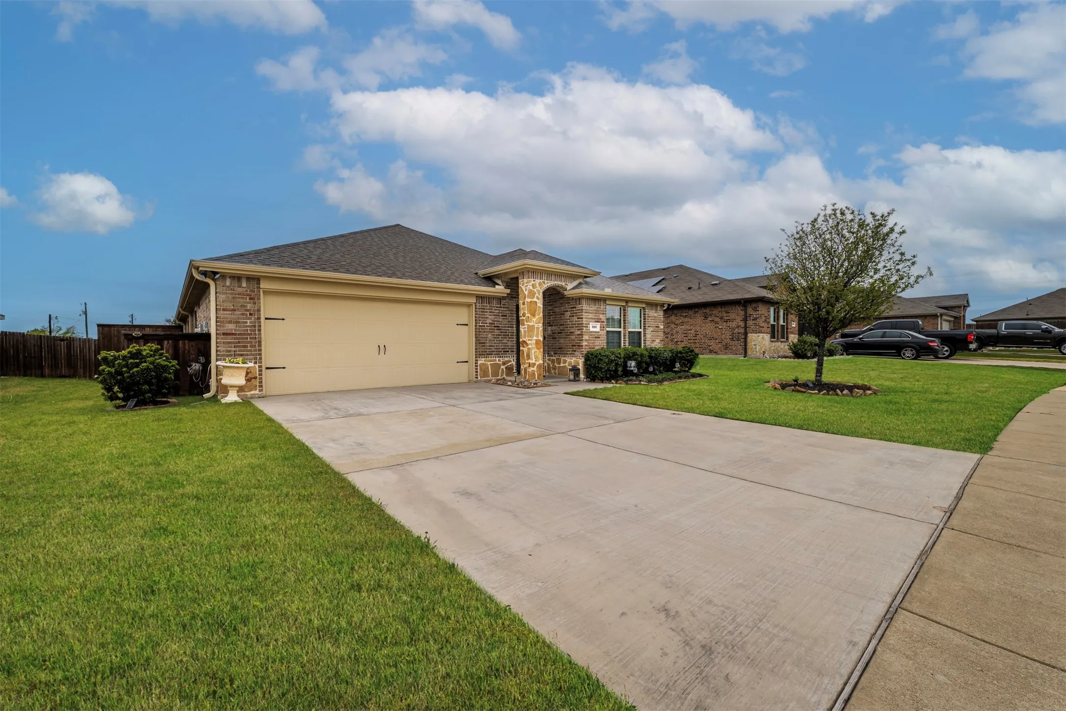 Brick and stone facade, attached garage, concrete driveway, and front lawn with mature tree