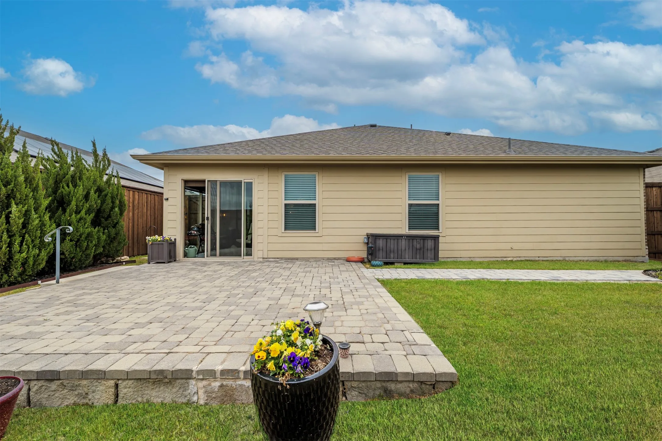 Expansive paver patio with a retaining wall, surrounded by a manicured lawn and mature shrubs