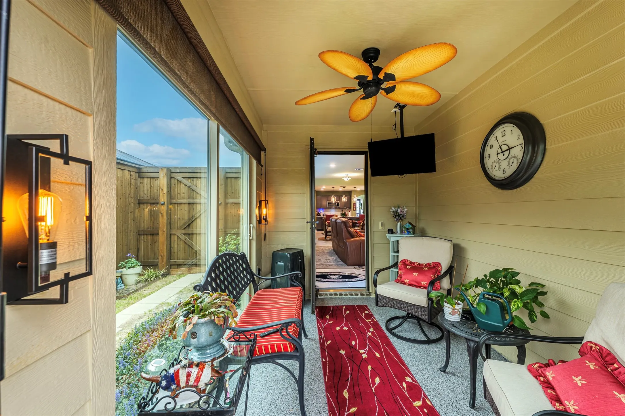 Enclosed outdoor space featuring a ceiling fan, wall-mounted light fixtures, full-length glass panels, and a wood fence