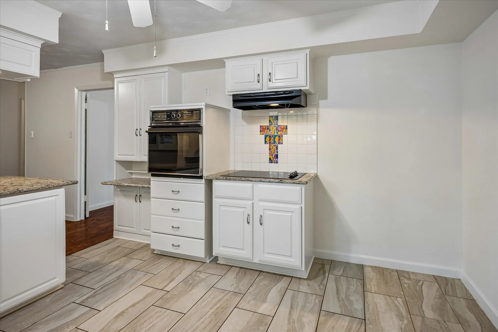Built-in oven, electric cooktop, white cabinetry, tile backsplash, and light-toned tile flooring