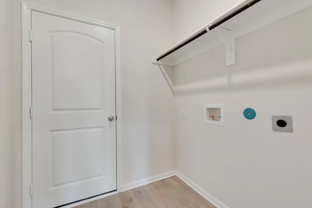 Utility area featuring light wood-finish flooring, white walls, built-in shelving, and a hanging rod