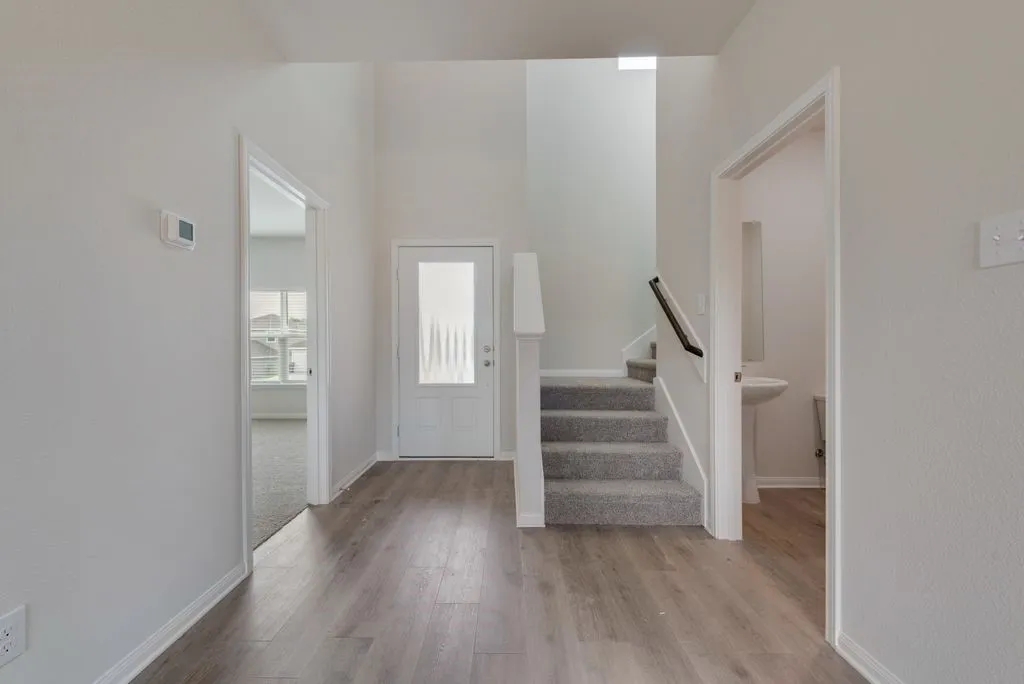 High ceilings, wood-finish flooring, carpeted staircase with handrail, pedestal sink, and frosted glass paneled door