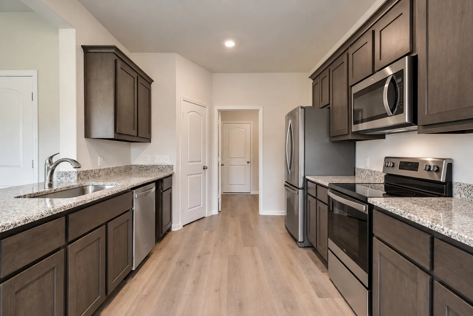 Galley kitchen featuring wood-finish flooring, dark wood cabinetry, light-toned stone countertops, a stainless steel sink, and stainless steel appliances
