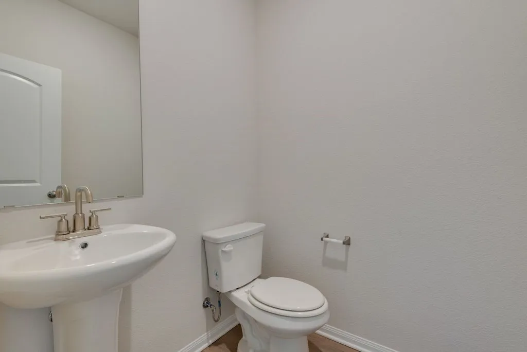 Pedestal sink with brushed nickel faucet, mirror, toilet, and wood-finish flooring