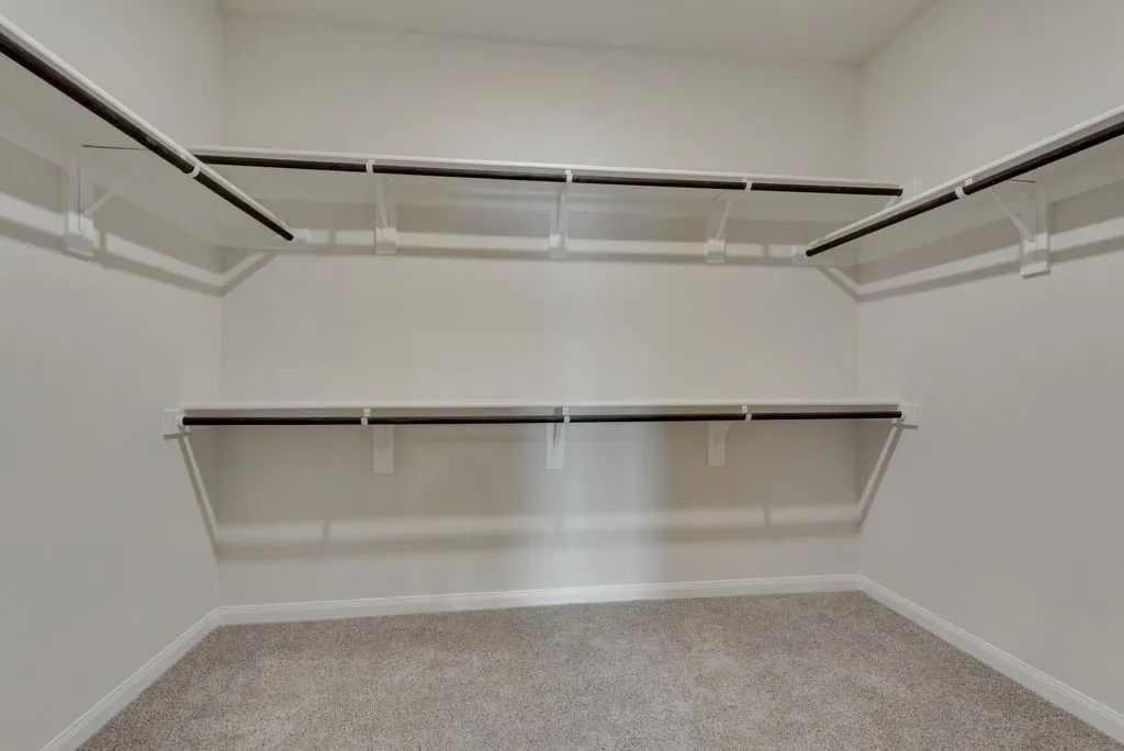 Walk-in closet featuring white shelving and hanging rods