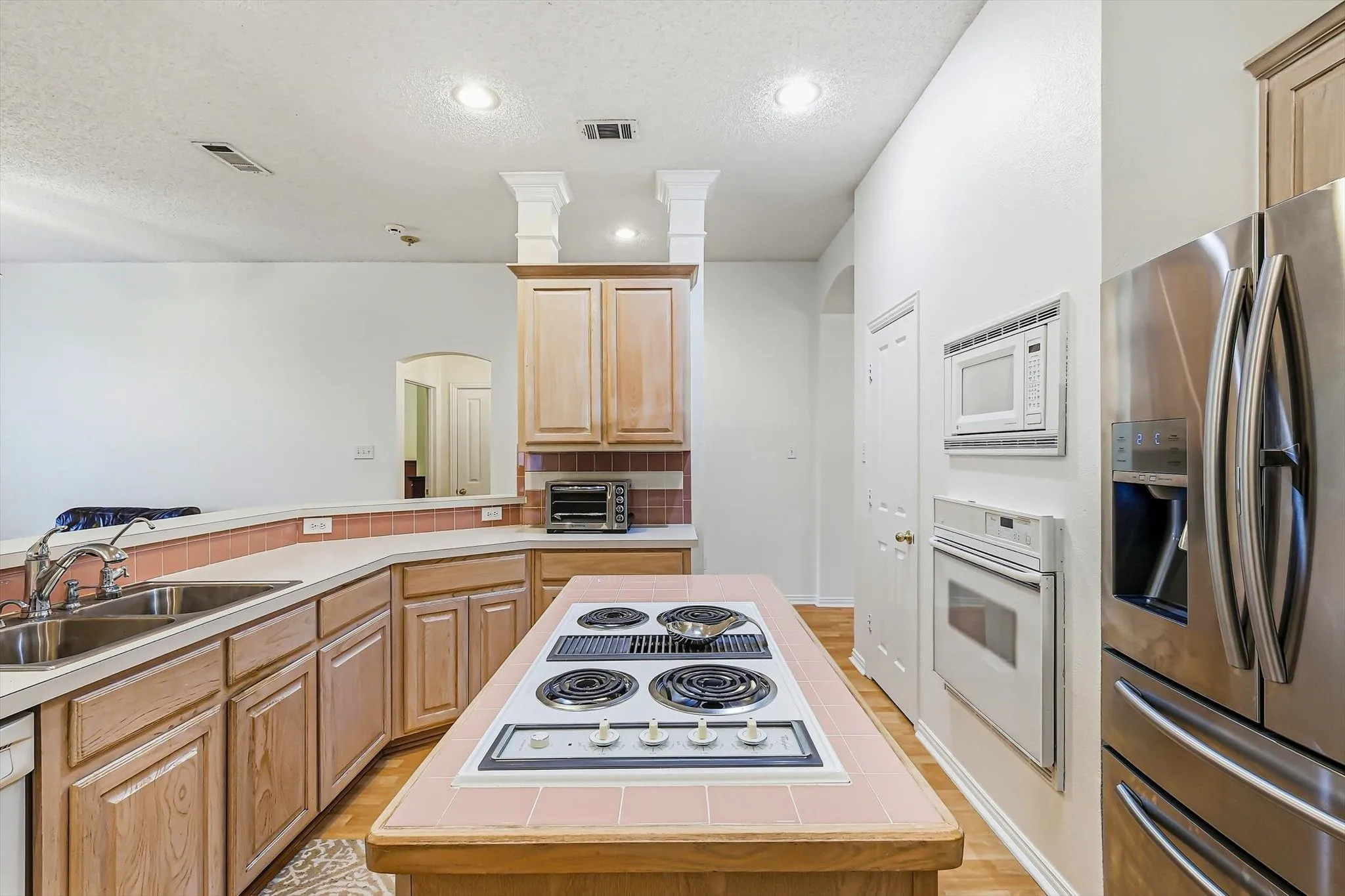 Kitchen with wood-finish cabinetry, stainless steel refrigerator, white built-in oven, and a tiled island cooktop