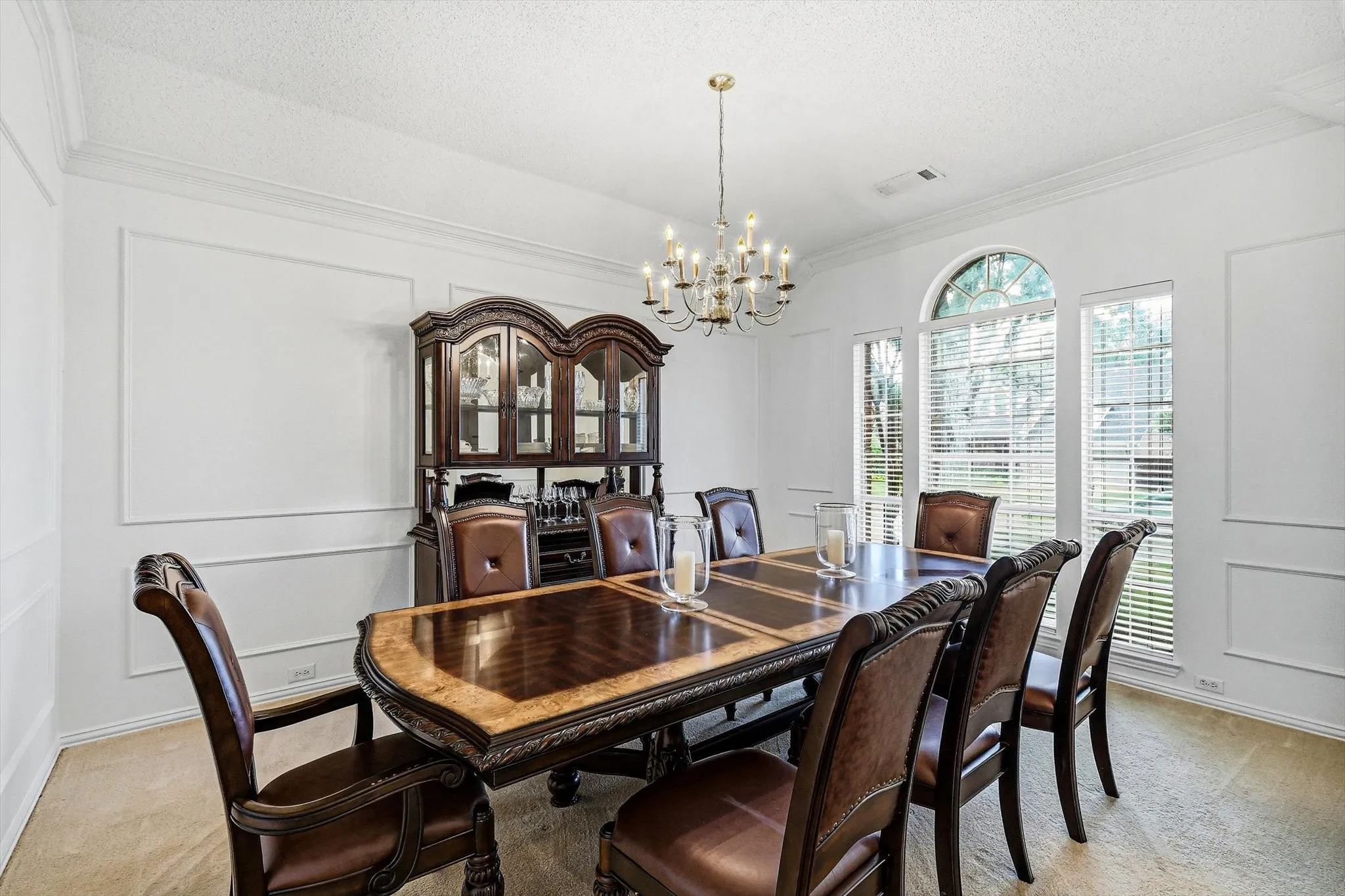 White walls with decorative trim molding, arched window, multiple vertical windows, and a brass chandelier