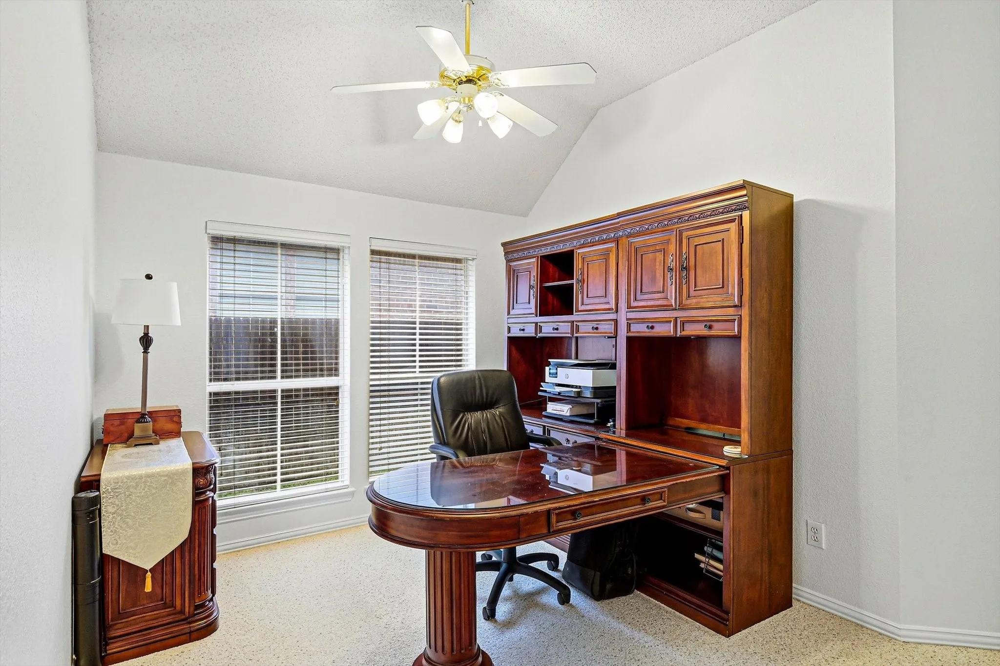Vaulted ceiling featuring a ceiling fan, two double-hung windows with blinds, and built-in cabinetry with a desk