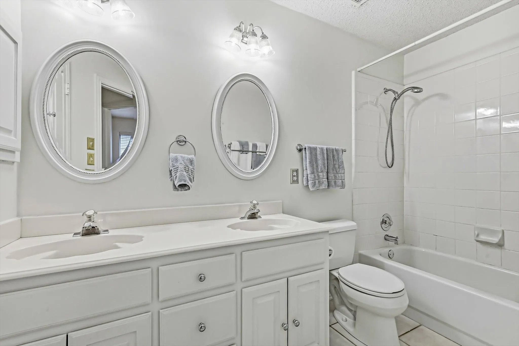 Dual oval mirrors, double vanity with integrated sinks, built-in cabinetry, and a full-size tub and shower combination with subway tile surround