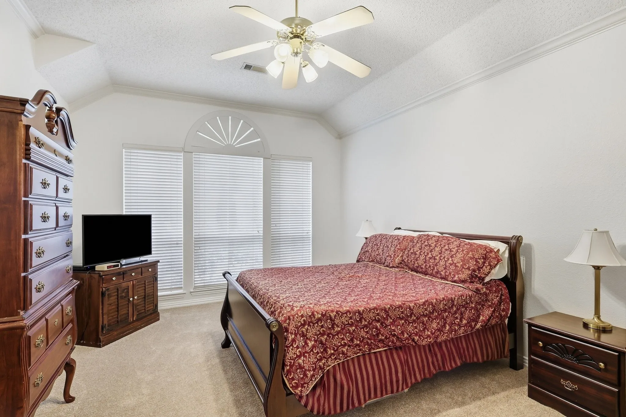 Vaulted ceiling with a ceiling fan, crown molding, arched window, and carpet flooring