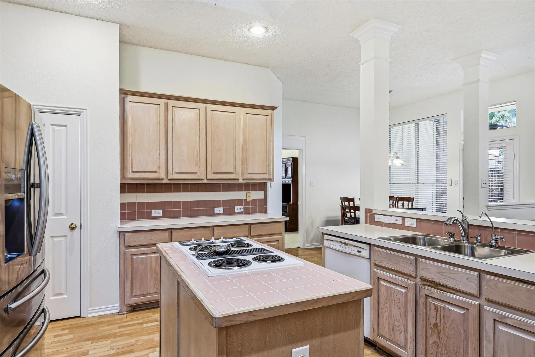 Kitchen featuring wood-finish cabinetry, tile backsplash, a center island with a cooktop, and a double basin sink
