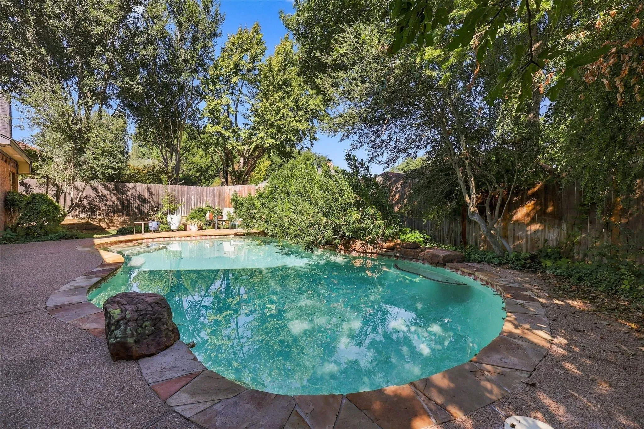Freeform swimming pool with a stone coping, surrounding concrete decking, and a privacy fence