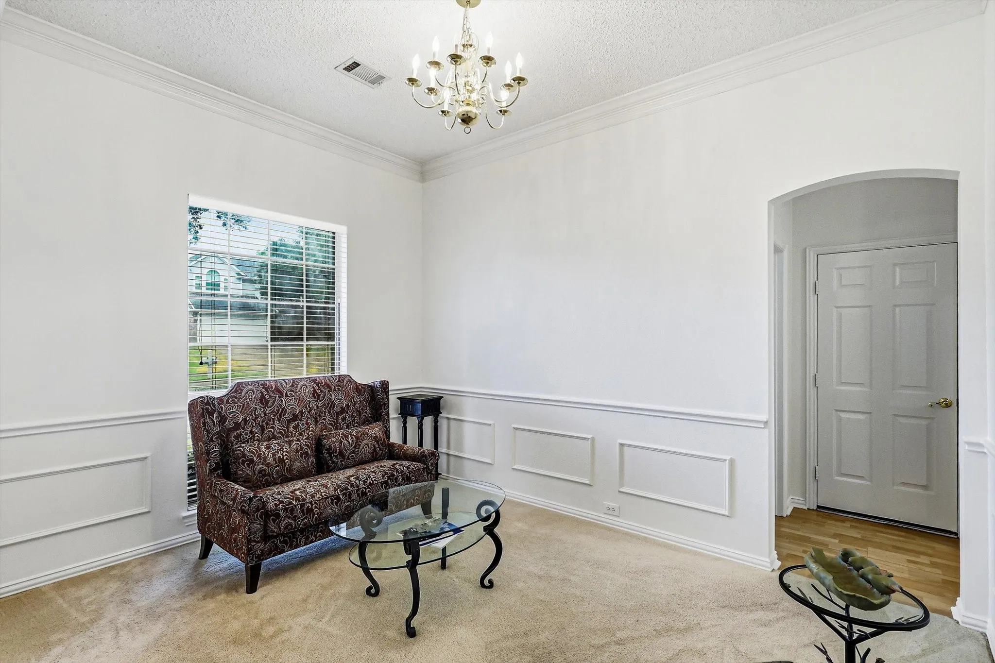 Wainscoting and crown molding details, decorative chandelier, arched doorway, and carpet flooring