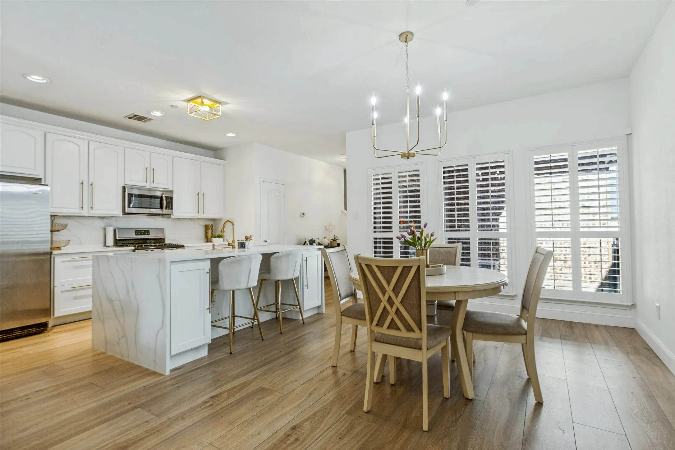 Contemporary kitchen featuring a large island with waterfall edge, white cabinetry, stainless steel appliances, and a gas range