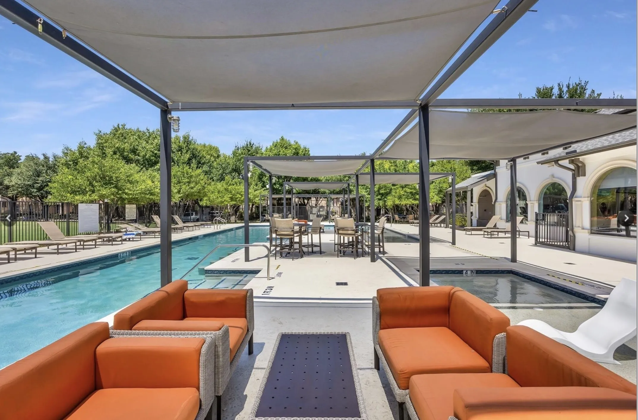 Expansive outdoor pool area featuring a long swimming pool, separate spa, and multiple shaded seating zones