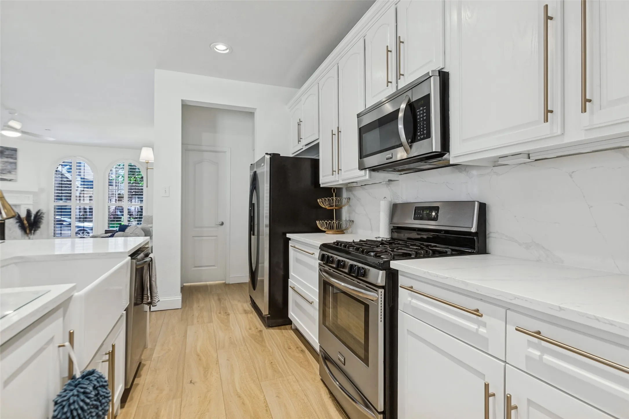 White cabinetry with gold-tone hardware, stainless steel appliances, and light-toned wood-finish flooring, Private half bath tucked away