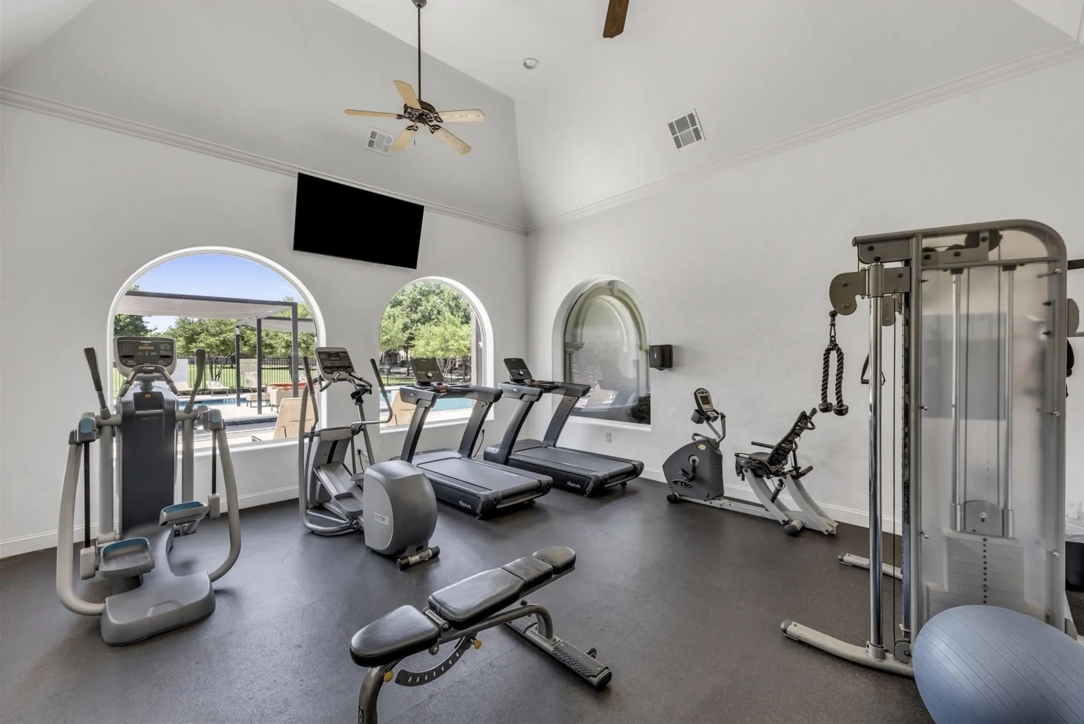 Fitness center featuring vaulted ceilings, arched windows, built-in television, and rubber flooring
