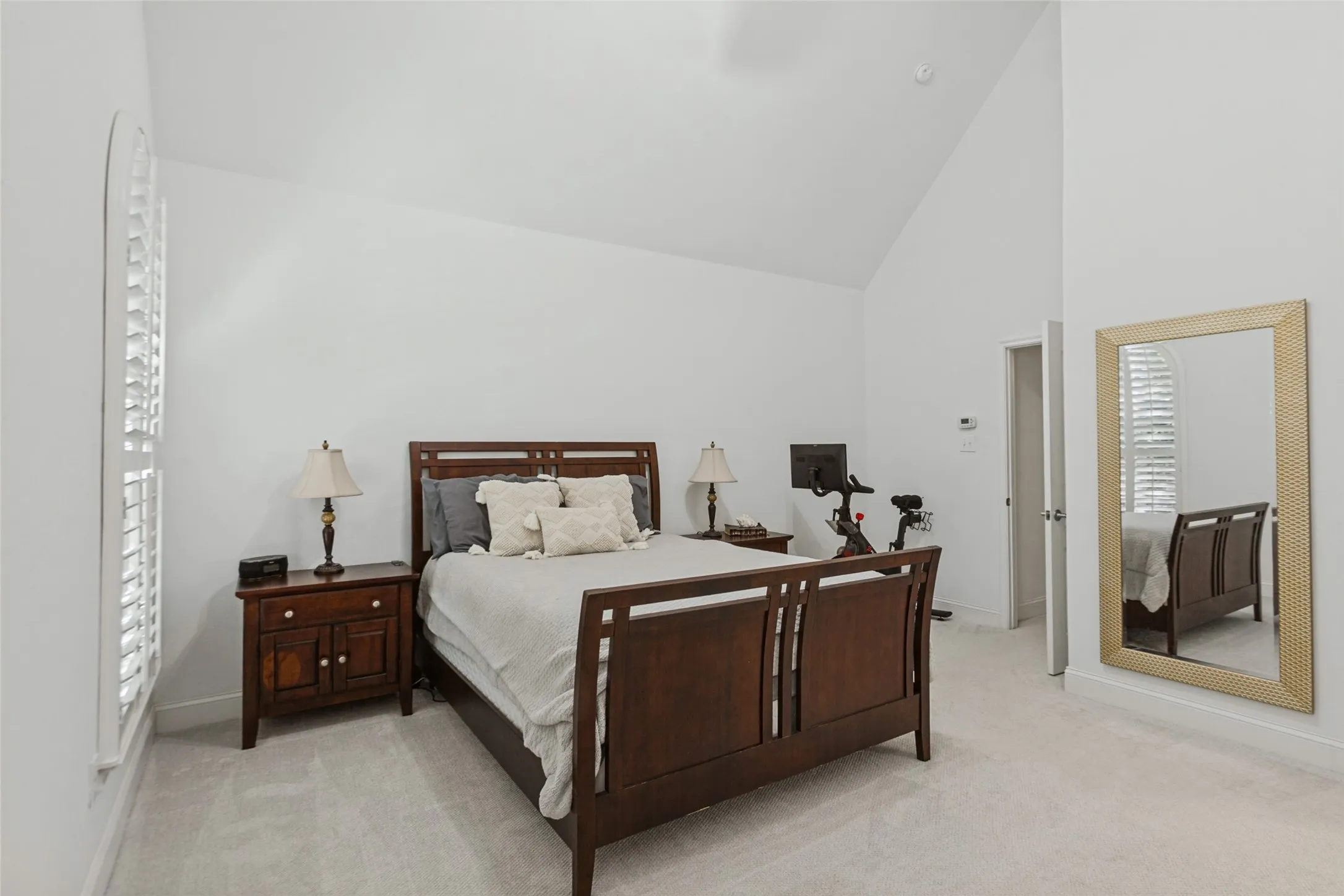 Primary bedroom with ensuite, Vaulted ceiling with a ceiling fan, white plantation shutters, and light-toned carpeting