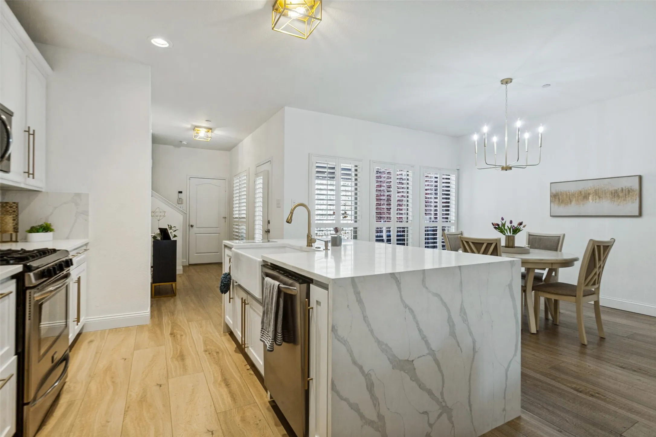 Open-concept kitchen and dining area featuring a waterfall island with an undermount farmhouse sink, stainless steel appliances, light wood-finish flooring, and white cabinetry