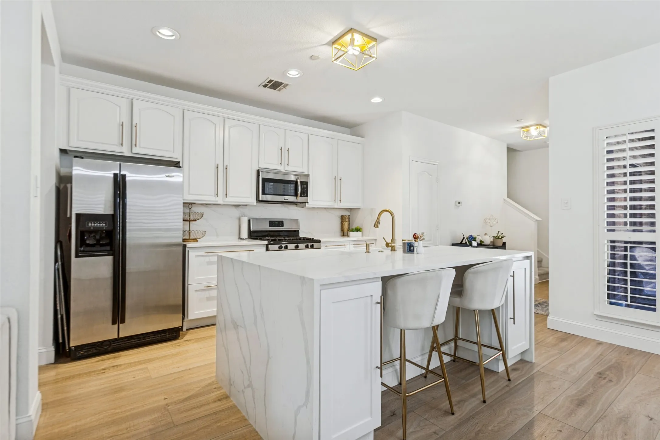 Gourmet kitchen featuring white custom cabinetry, stainless steel appliances, a center island with waterfall-edge quartz countertop, and wide luxury vinyl plank wood-finish flooring