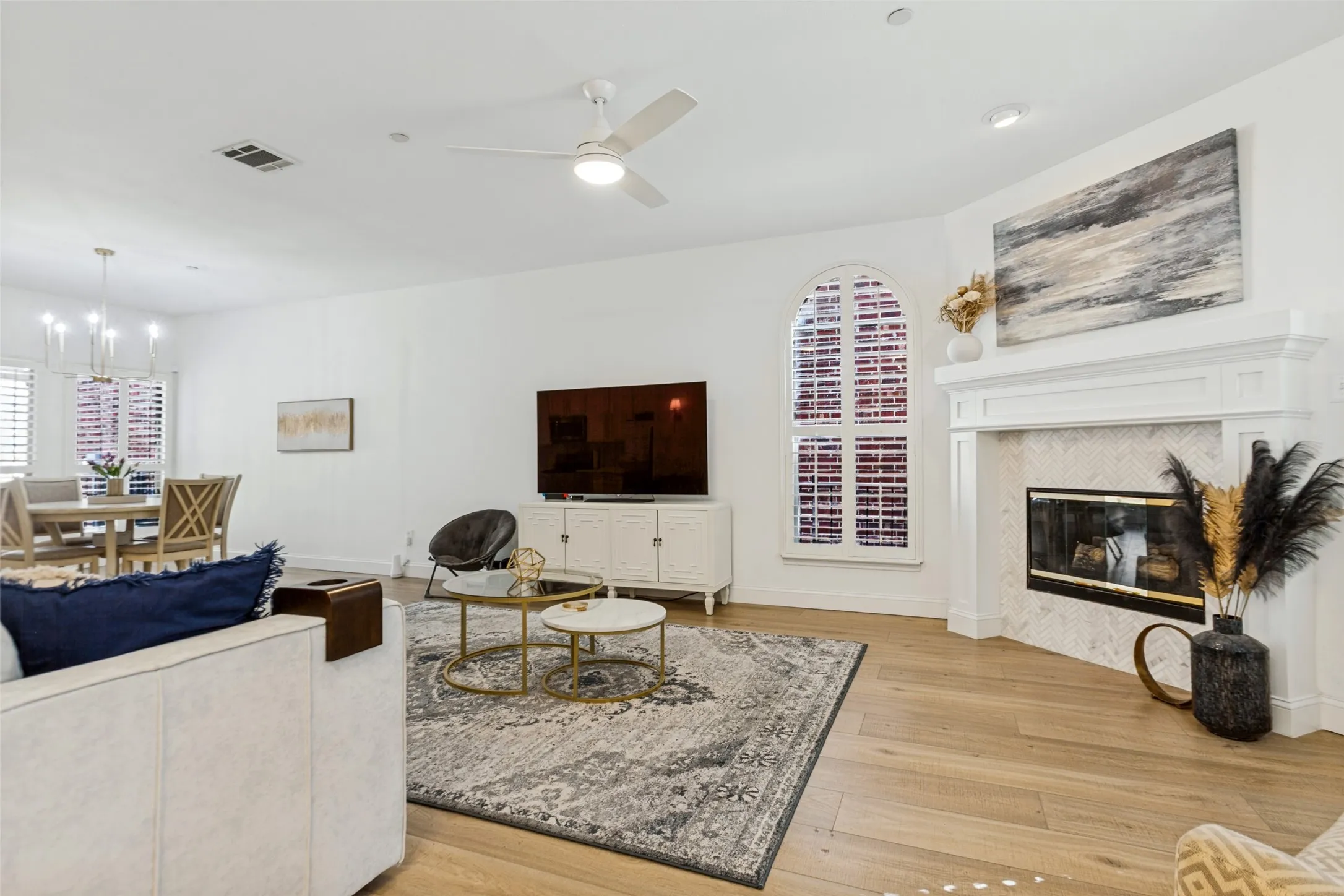 Light colored Luxury vinyl plank flooring throughout, a gas fireplace with a tiled surround, a costume wood decorative mantel, and an arched window with plantation shutters