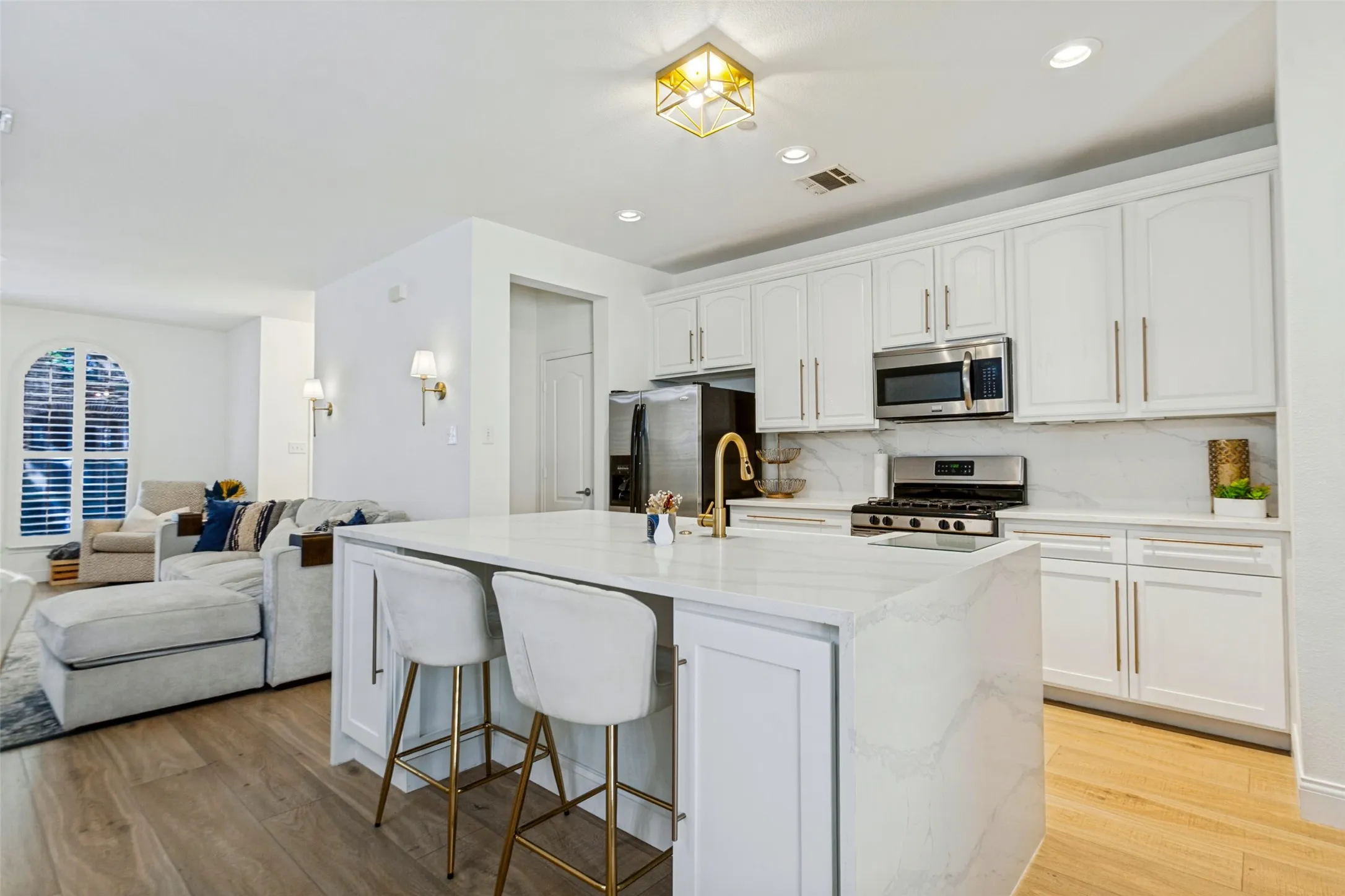 Open-concept kitchen with white cabinetry, stainless steel appliances, and a central island featuring a gold-finish faucet