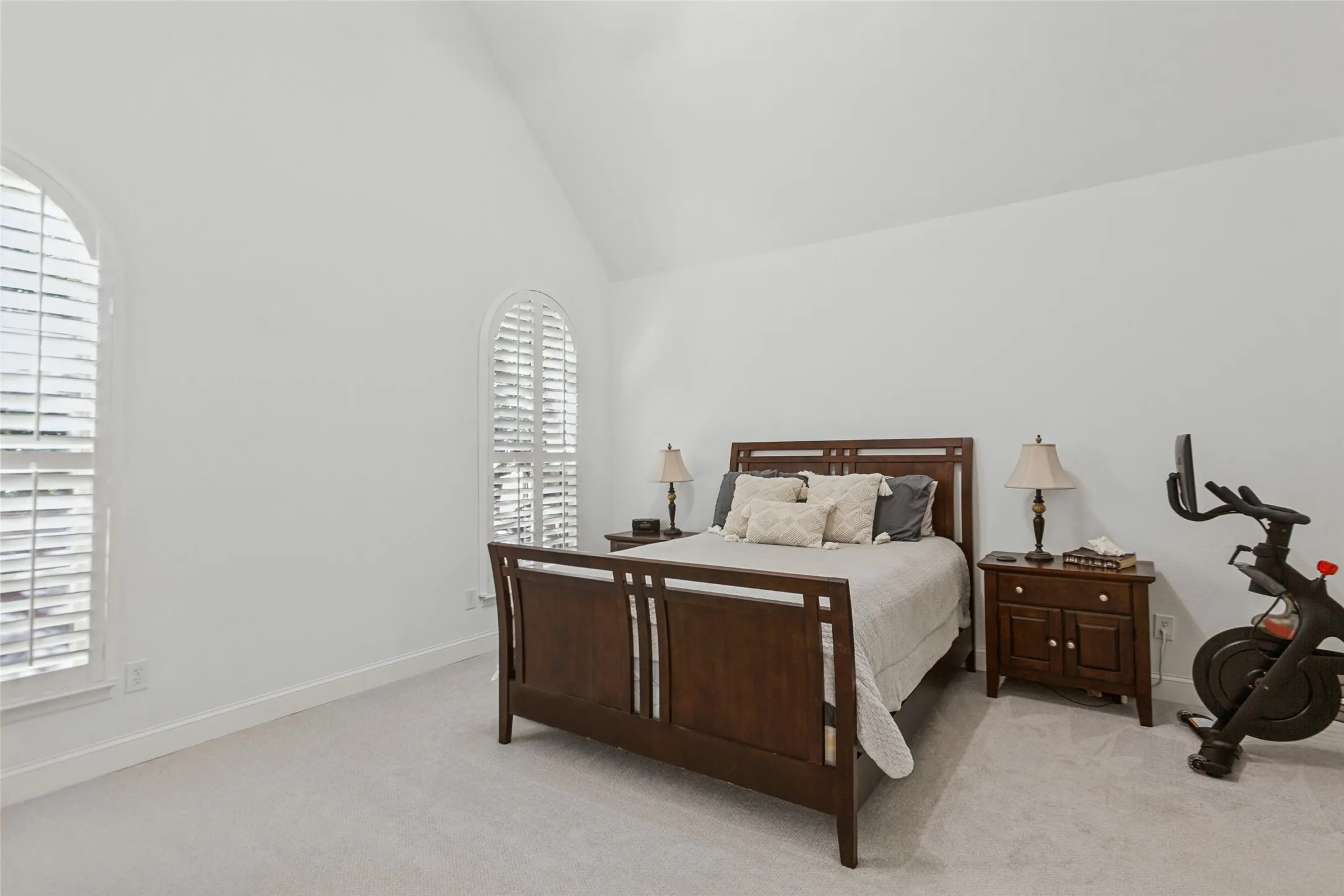 Primary Suite featuring Vaulted ceiling, arched windows with plantation shutters, light-toned carpeting, and white wall finishes