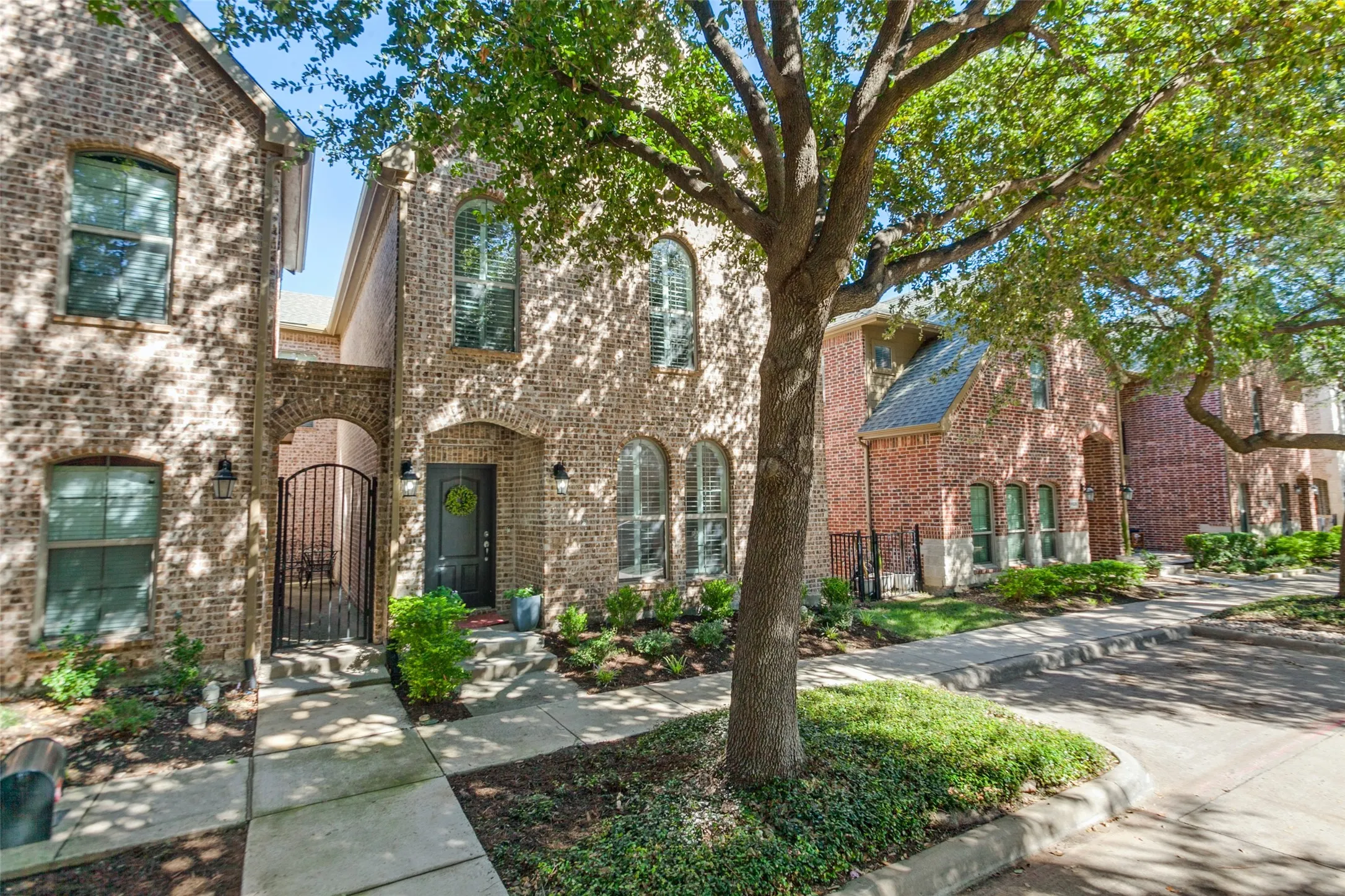 Brick exterior featuring arched windows with shutters, a stone walkway, and established trees with additional guest street parking