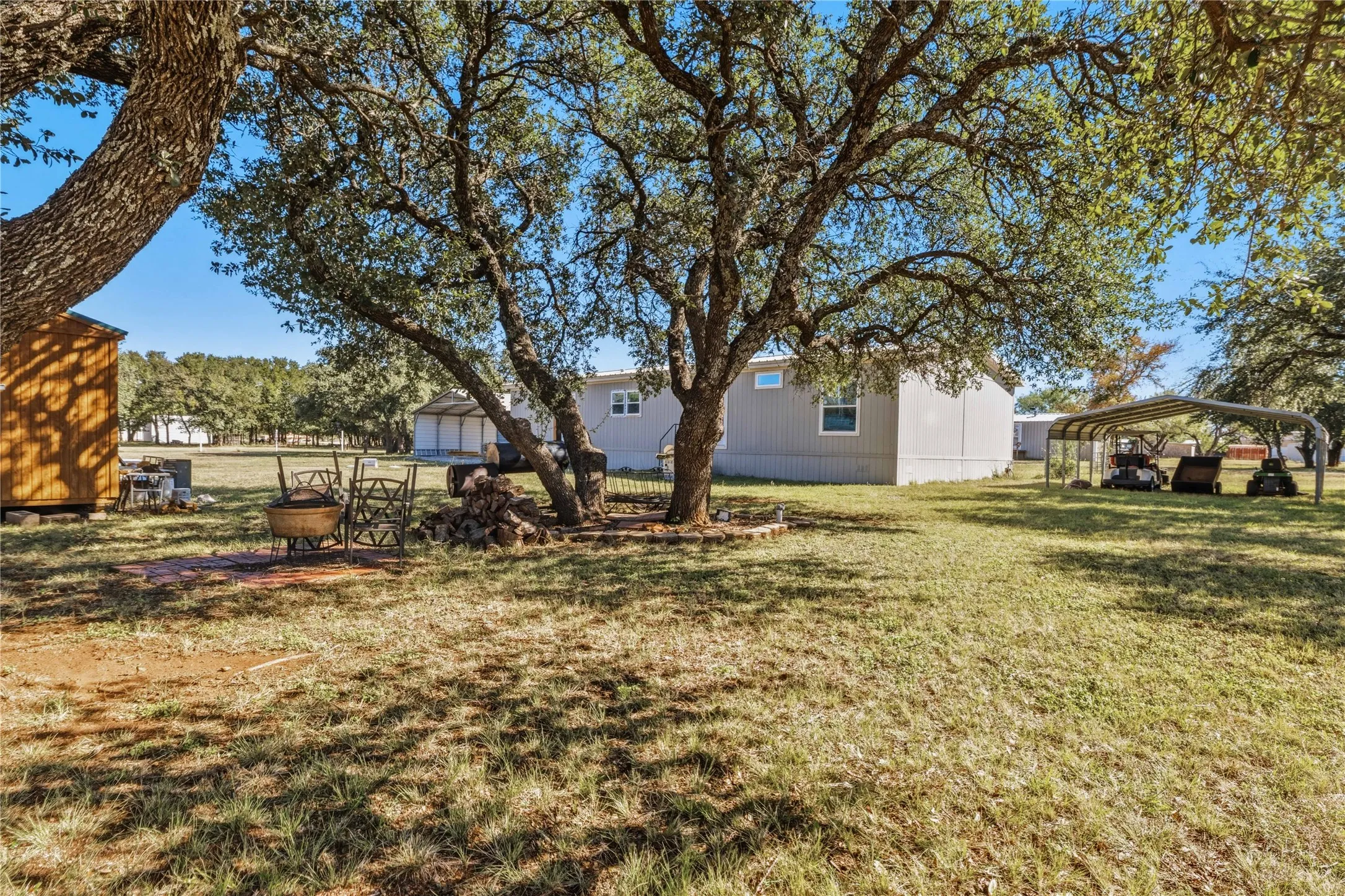 Expansive grassy yard with mature trees, a detached storage shed, and a metal carport