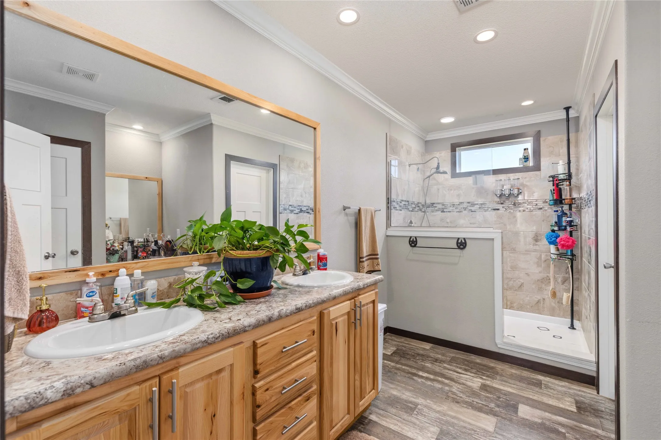 Double vanity with wood-finish cabinetry, a framed mirror, and wood-finish flooring