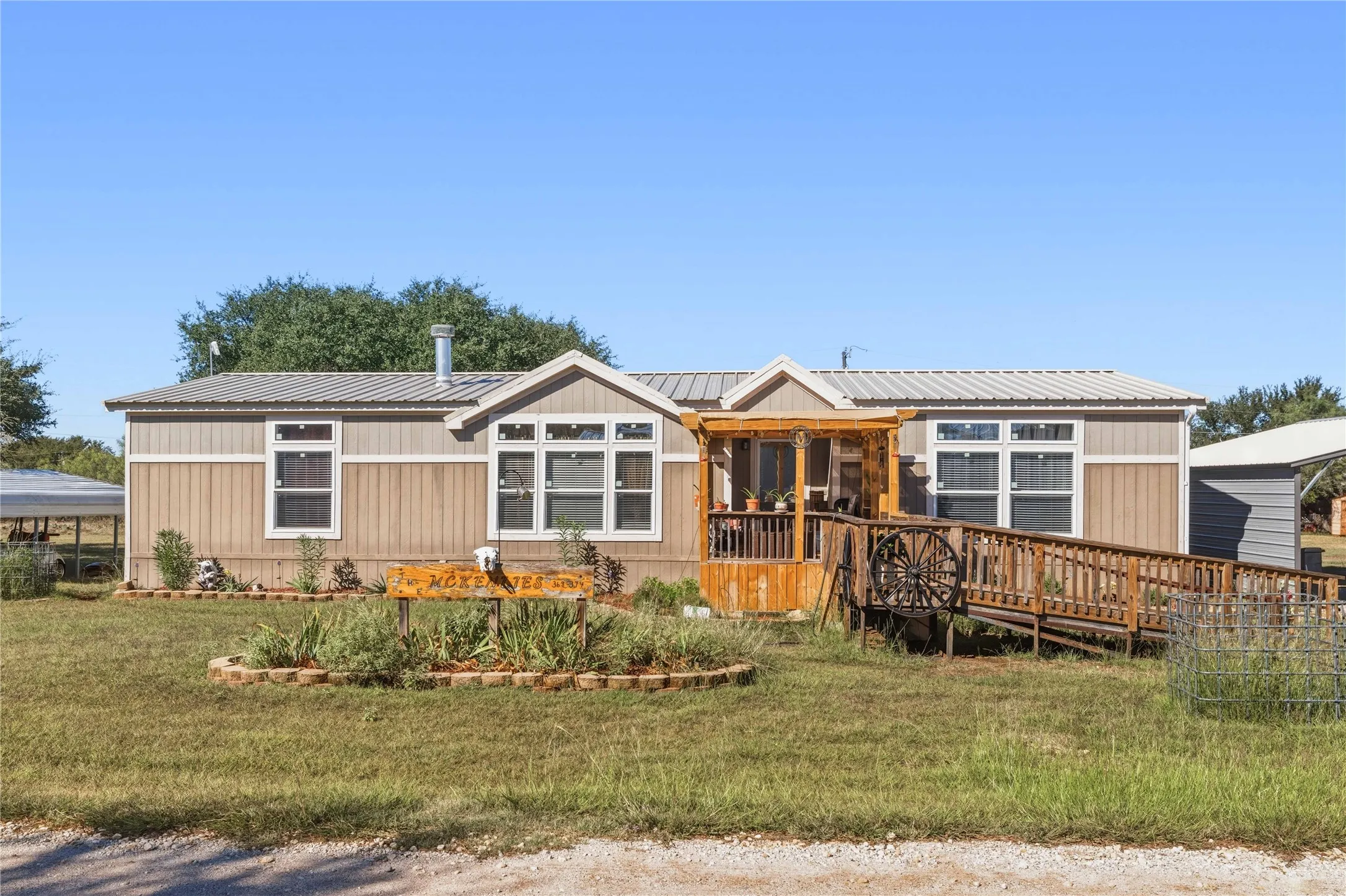 Two-tone exterior siding, metal roof, covered porch, wooden ramp access, and landscaped front yard