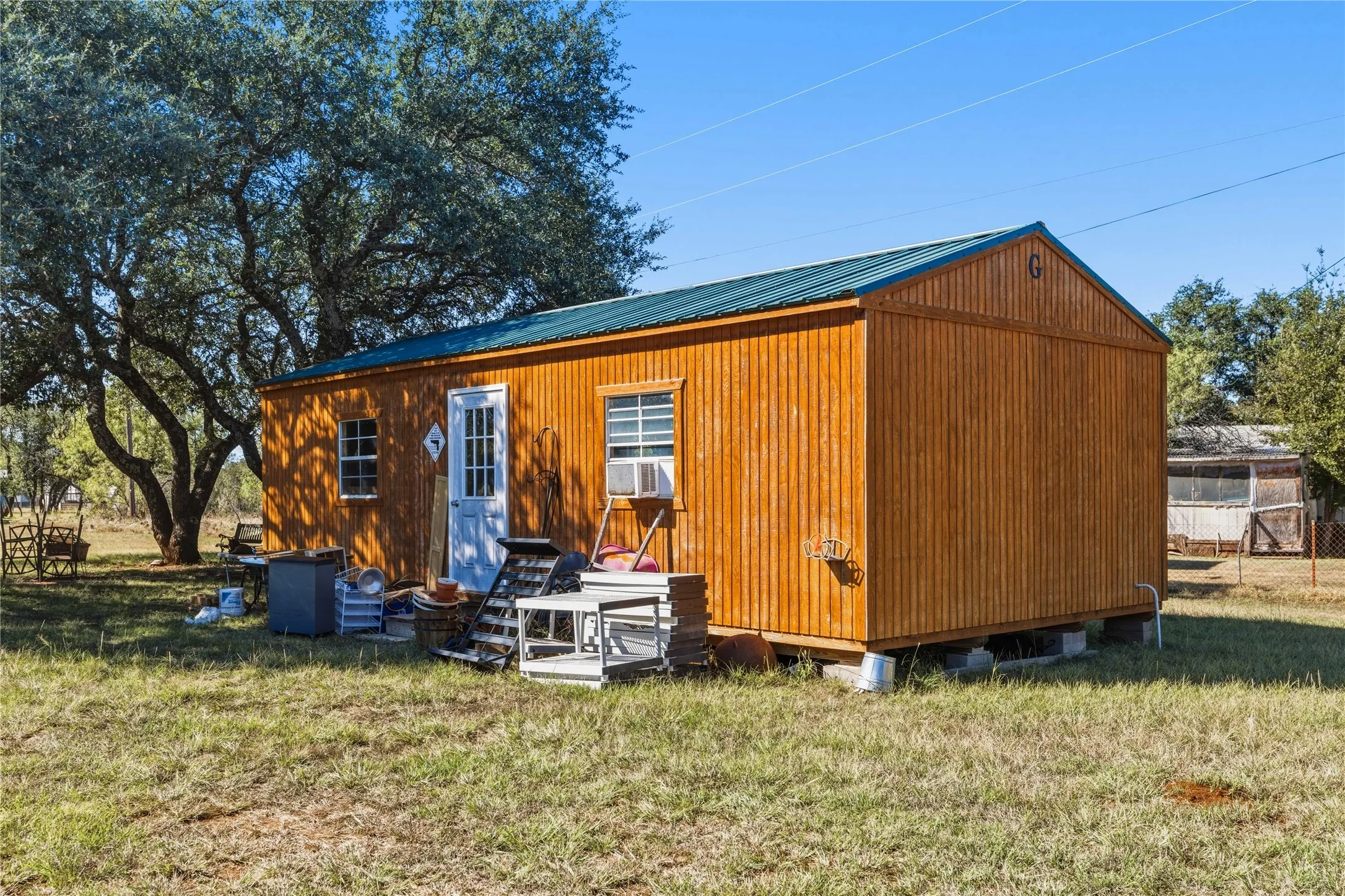 Wood-sided structure with a green metal roof, multiple windows, and an exterior door