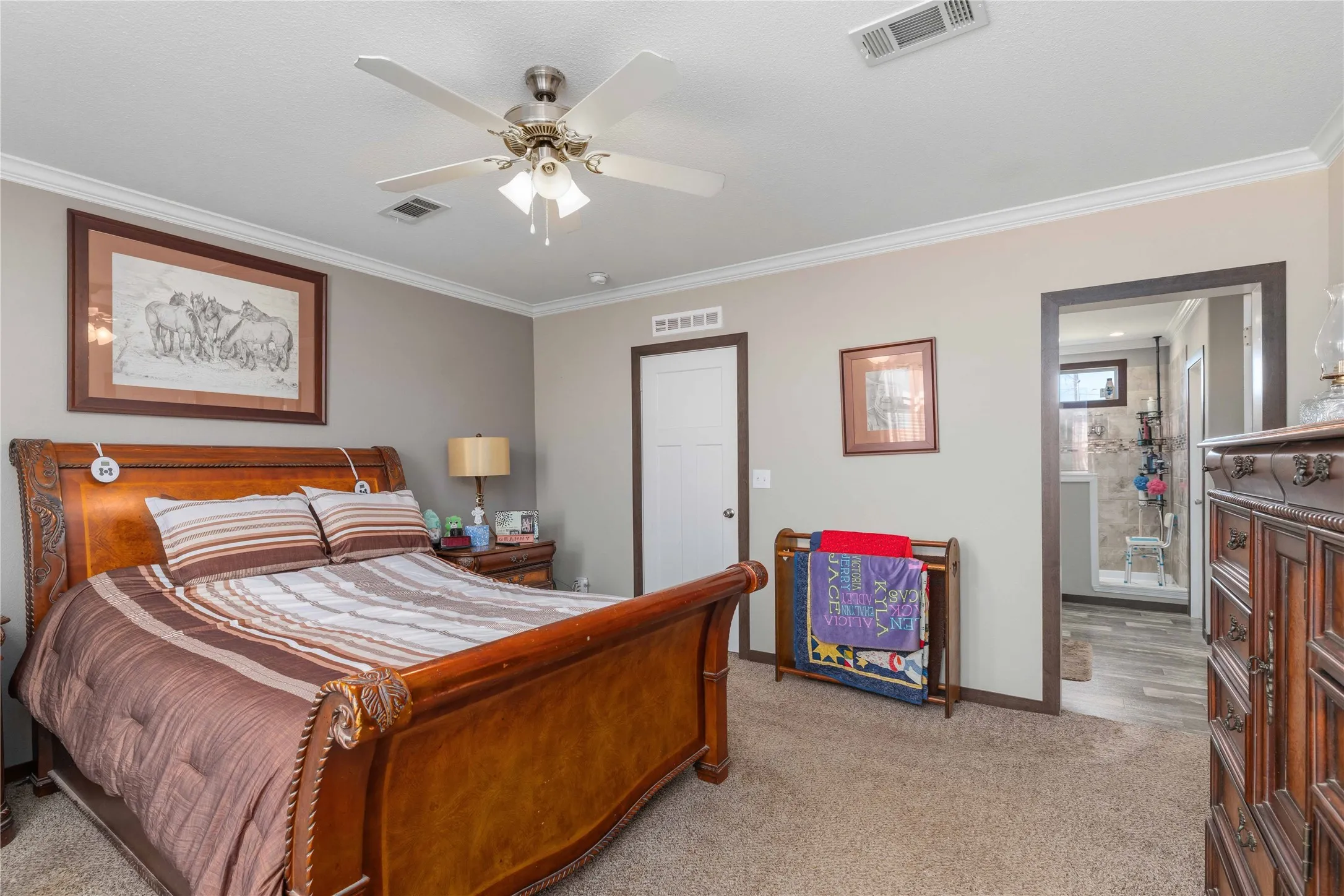 Carpeted flooring, crown molding, ceiling fan with integrated lighting, and a doorway leading to a tiled bathroom with a glass-enclosed shower