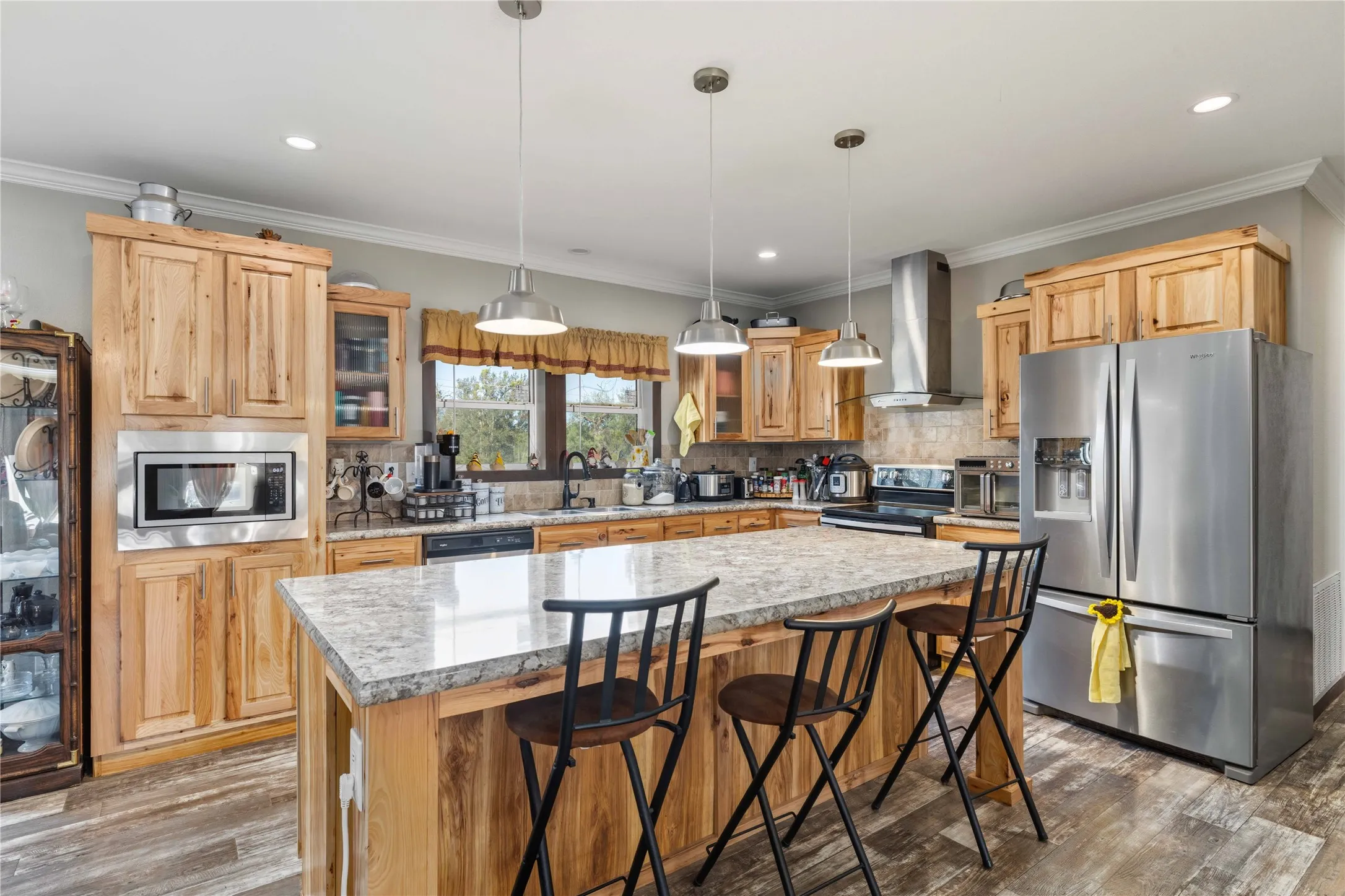 Expansive kitchen featuring wood-finish cabinetry, stainless steel appliances, a large island with a light-toned countertop, and recessed lighting
