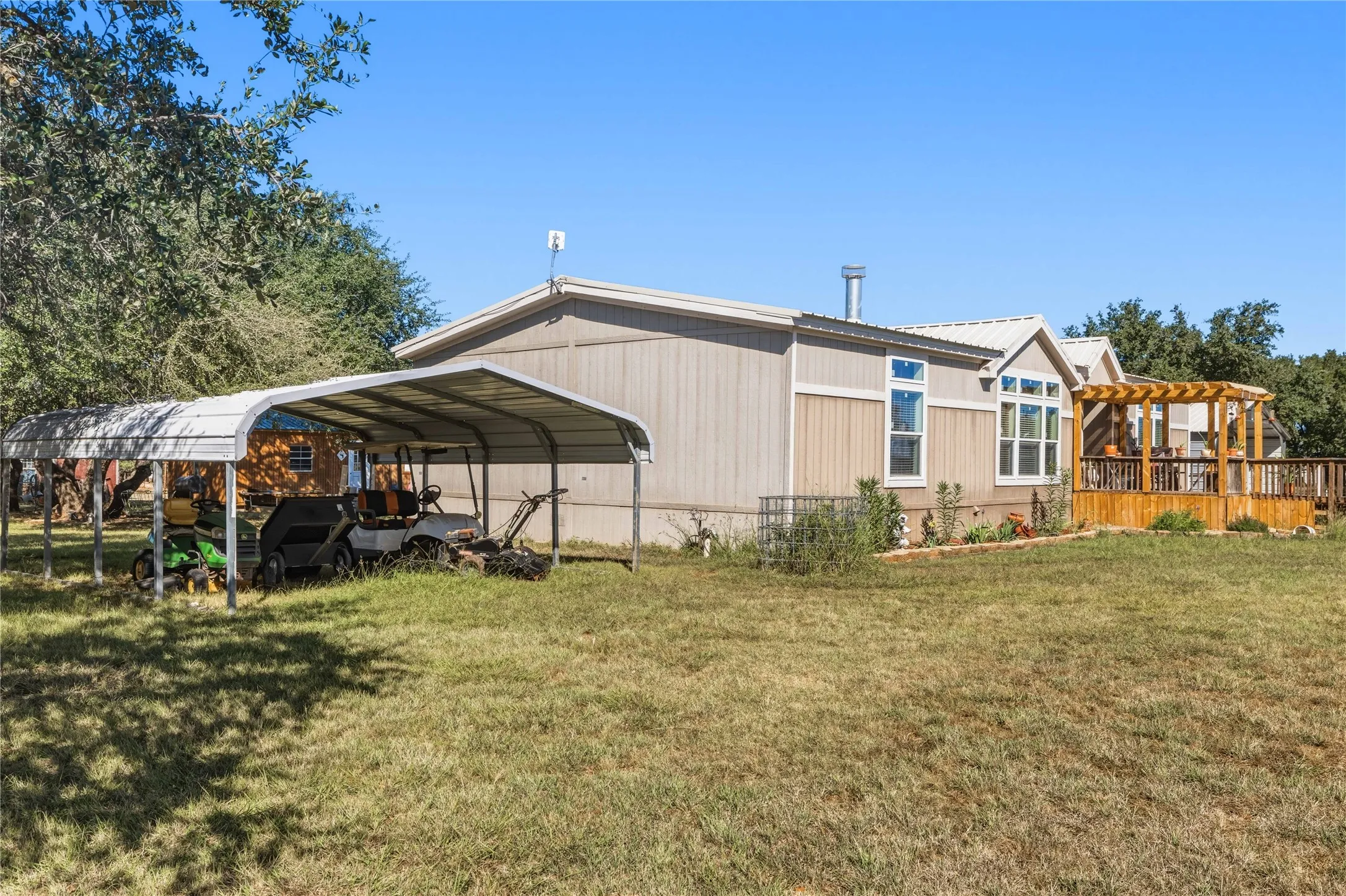 Expansive outdoor decking with a wood pergola, multiple large windows, and a detached metal carport