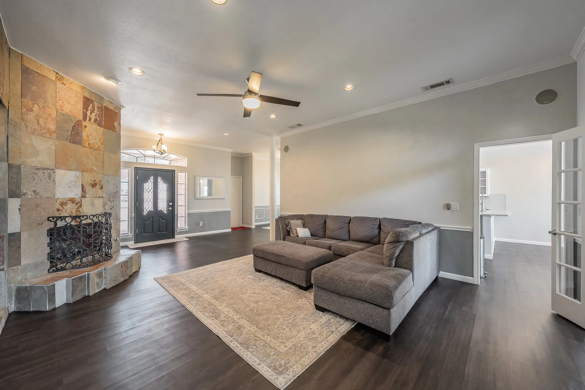 Spacious interior with dark wood-finish flooring, a stone fireplace, recessed lighting, crown molding, and a ceiling fan