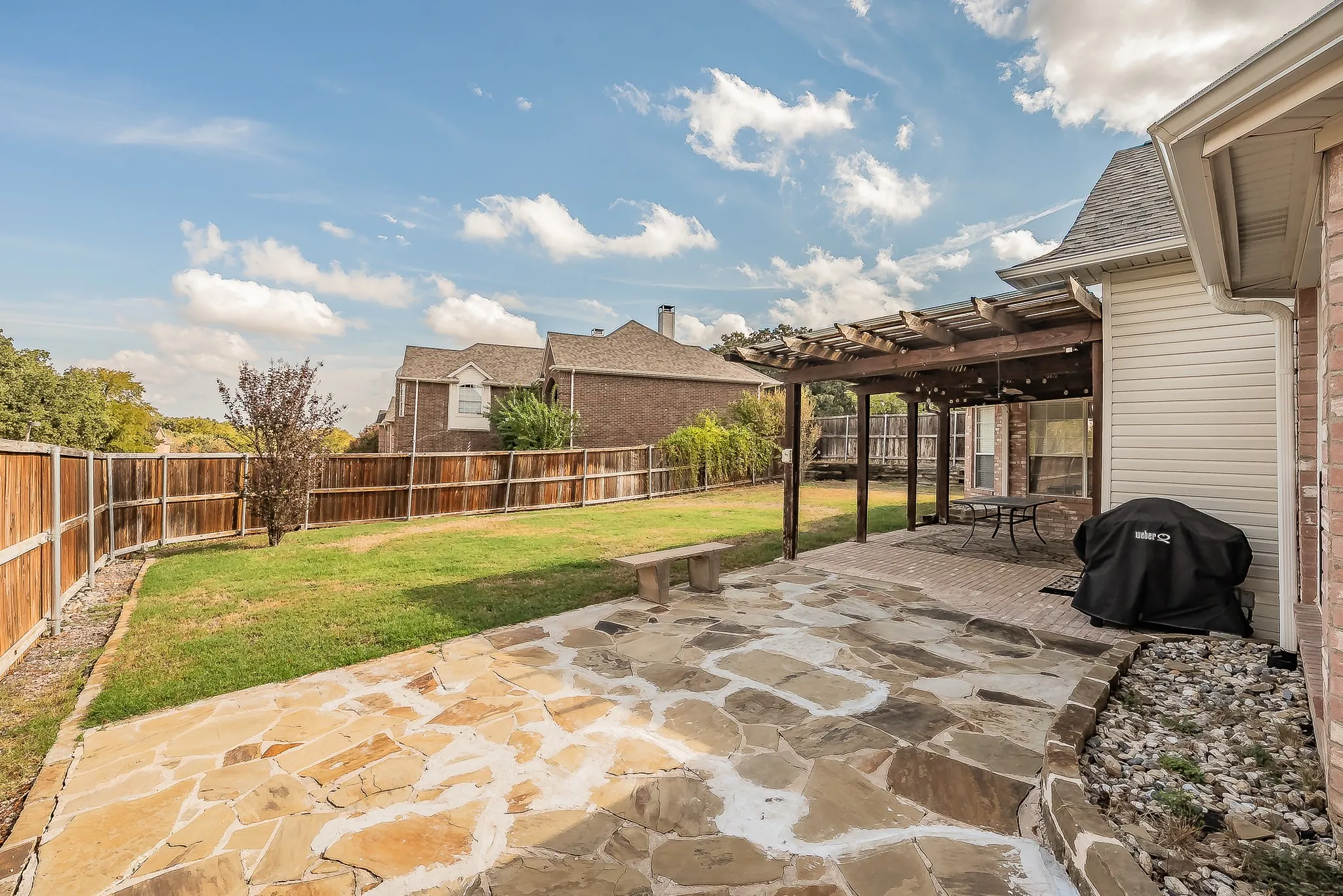 Expansive backyard featuring a full wood privacy fence, a flagstone patio, a covered brick patio, and a wooden pergola structure