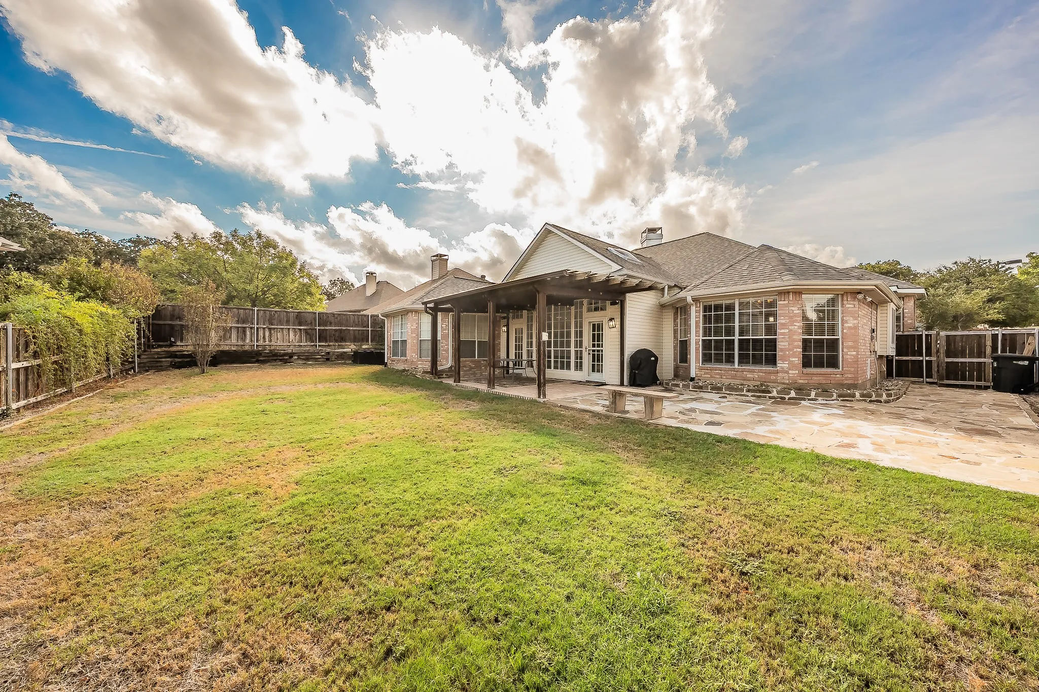 Expansive backyard featuring a stone patio, covered pergola, and a full privacy fence