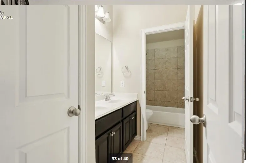 Dual sink vanity with dark wood-finish cabinetry, a large wall-mounted mirror, and tile flooring