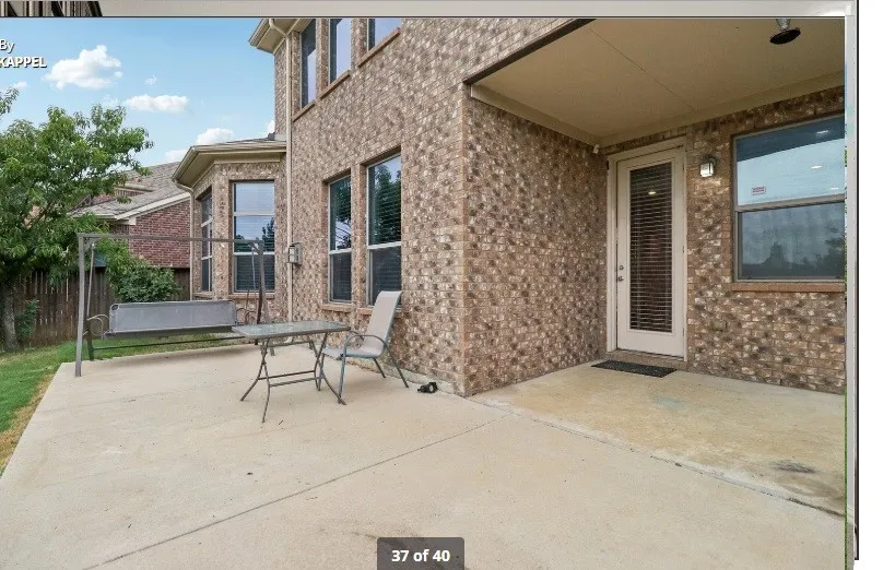 Expansive concrete patio with a covered section, brick exterior, and multiple windows