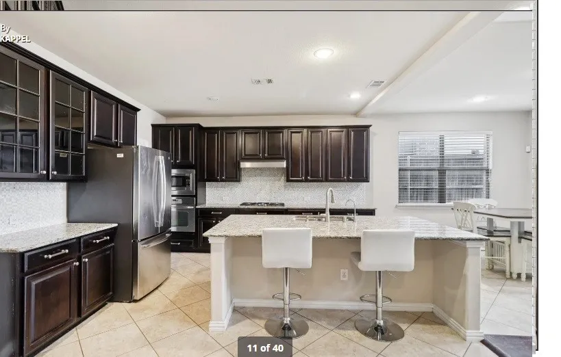 Kitchen featuring dark wood-finish cabinetry, light-colored countertops, stainless steel appliances, and a central island with an integrated sink