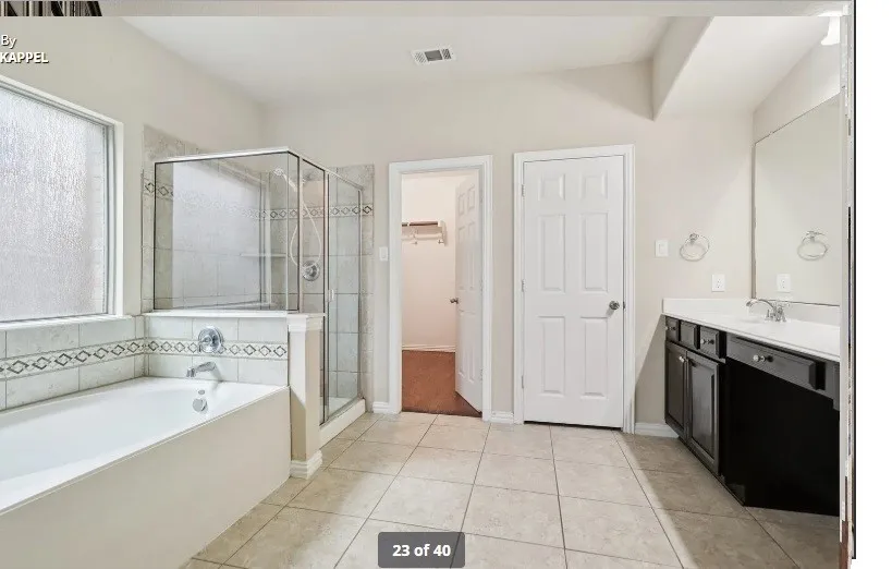 Integrated soaking tub with tiled surround, separate glass-enclosed shower, large vanity with dual sinks, and tile flooring