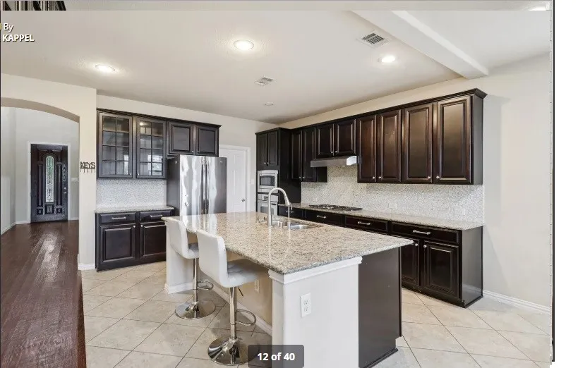 Kitchen featuring dark wood-finish cabinetry, light-toned tile flooring, recessed lighting, a central island with a light-toned countertop, and stainless steel appliances